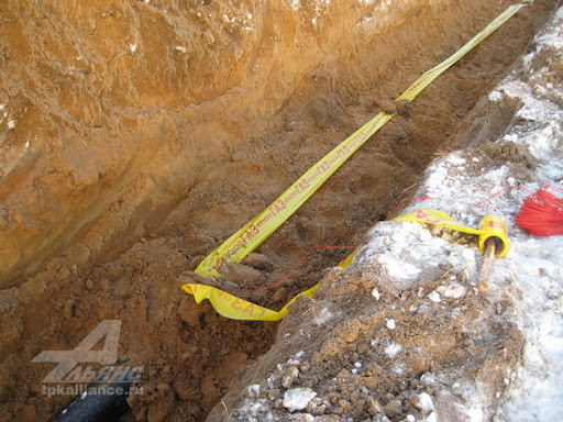 Сигнальная лента для маркировки подземных коммуникаций Желтая сигнальная лента с надписью, обозначающая подземные коммуникации, расположена в траншее, покрытой грунтом.